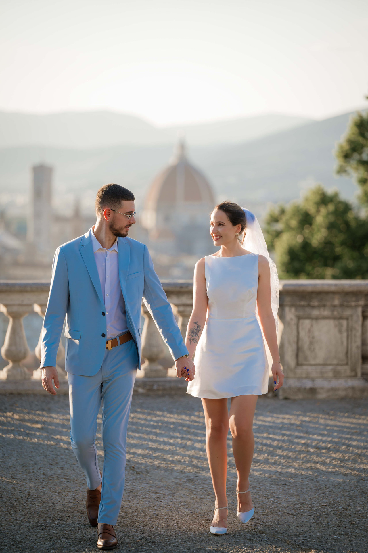 Bride and groom walking hand in hand at Piazzale Michelangelo, with the Duomo of Florence behind them